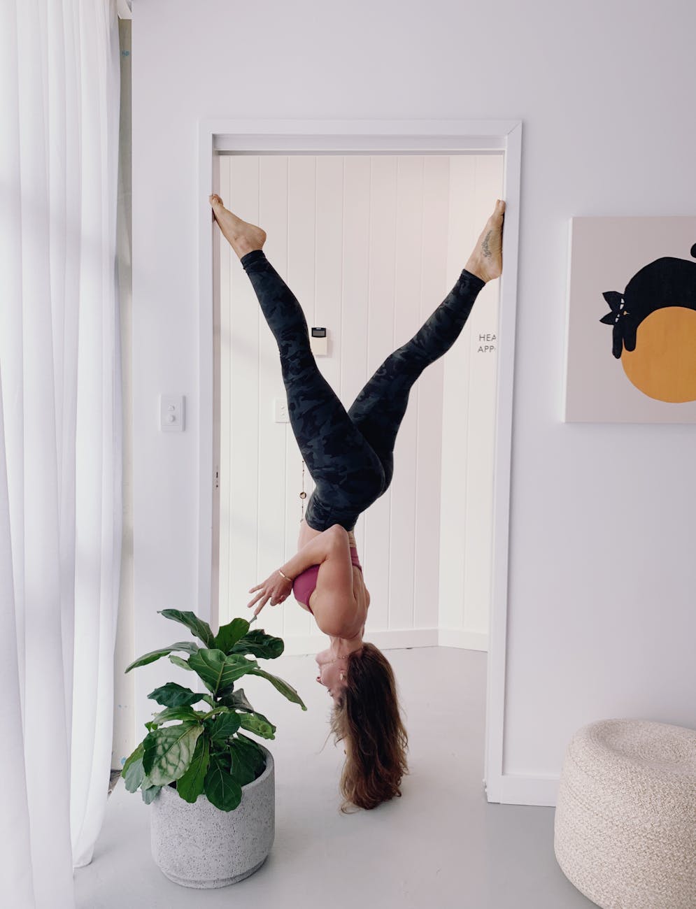 woman in workout gear hanging upside down on doorway near green plants